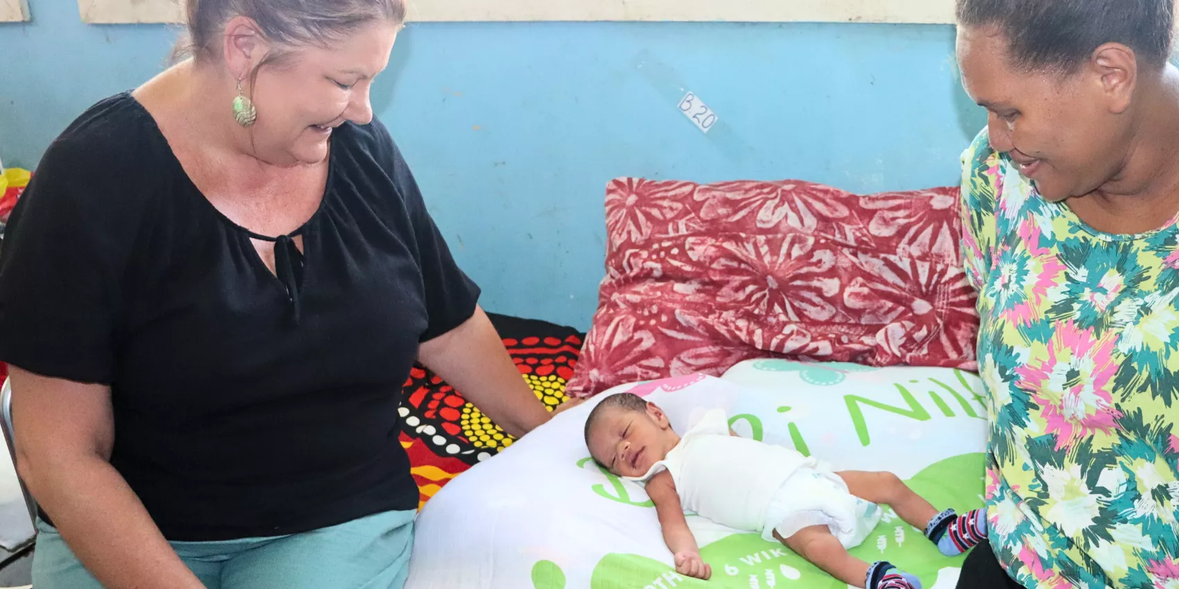 Immunisation message on a swaddle blanket in the Solomon Islands, Immunisation project person pictured left, baby pictured middle and mother of baby pictured right
