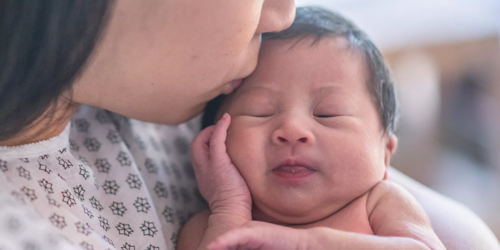 A newborn baby in the arms of a mother wearing a hospital gown