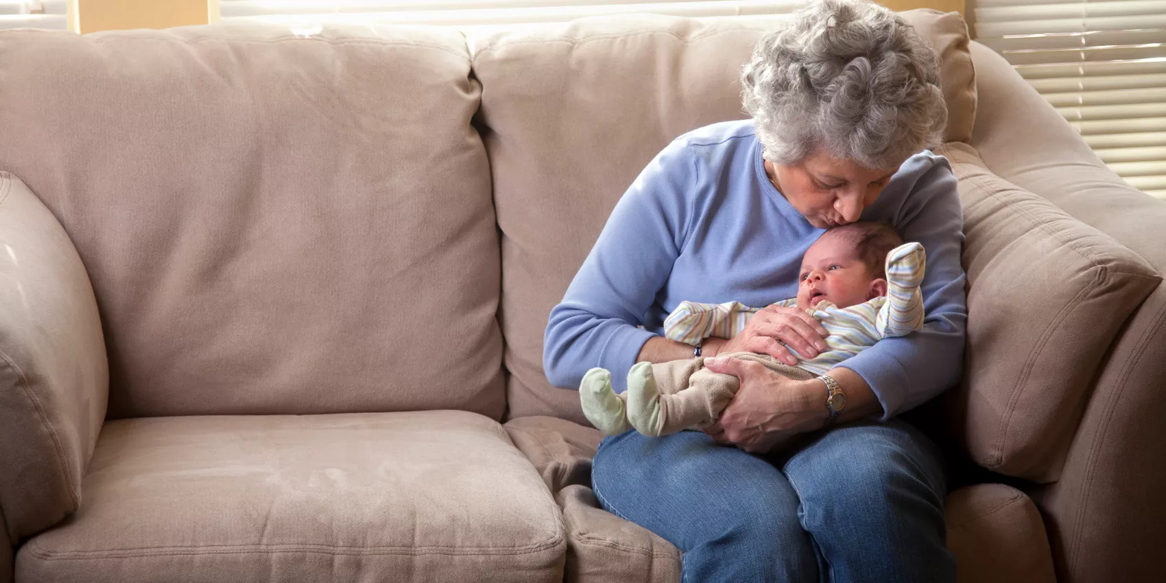 A young newborn gets a kiss from his grandma while sitting on a couch